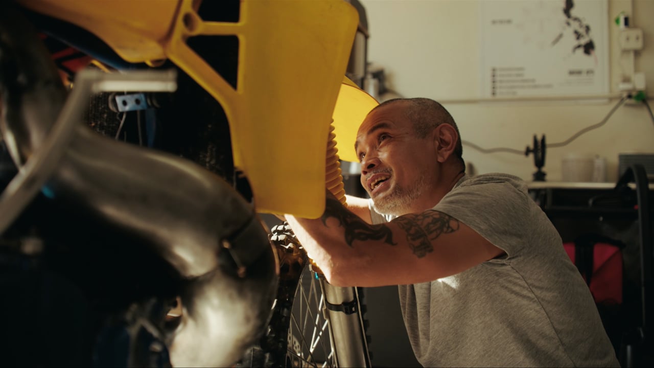 Bike builder Noel Ojerio working on a yellow dirt bike in his shop, from Never Standard
