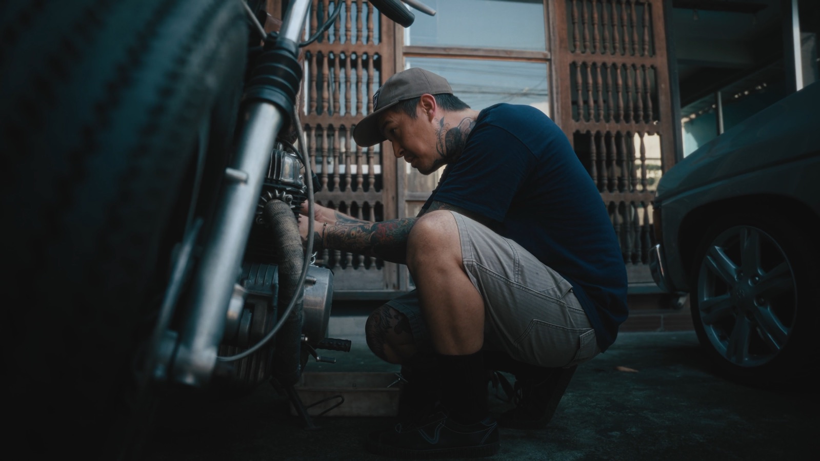 Matt crouched beside a motorcycle on the street outside his shop